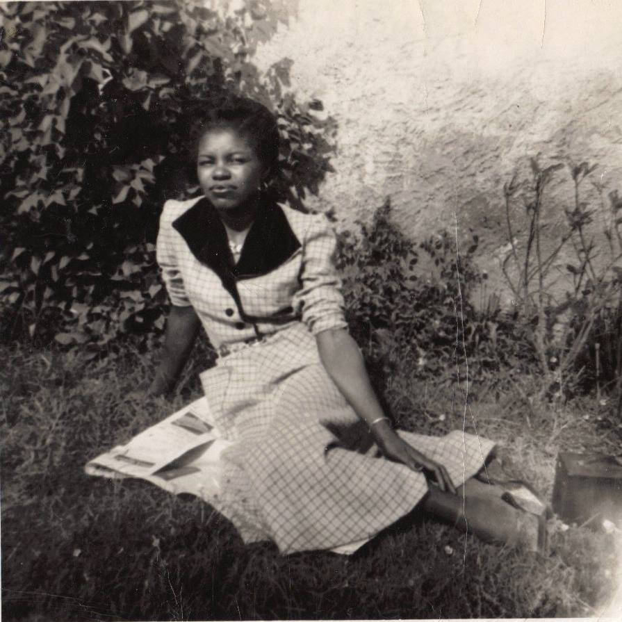 Young Miss Lucille sitting in a garden wearing a checkered dress with dark collar